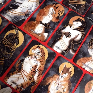 Puede incluir: Un juego de cartas de tarot con personajes de animales antropomorfos en varias poses. Las cartas son negras con detalles dorados y tienen un fondo estrellado. Las cartas incluyen "Ocho de Aire", "XII | El Ahorcado", "Reina de Aire", "Siete de Aire", "Cuatro de Aire", "Diez de Fuego", "Cinco de Fuego" y "Caballero de Fuego".