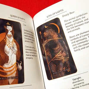 Puede incluir: Dos cartas de tarot, Reina de la Tierra y Rey de la Tierra, con ilustraciones de una vaca y un oso grizzly. La carta de la Reina de la Tierra tiene un texto que dice "Simb&oacute;lico de la nutrici&oacute;n y de poner las necesidades de los dem&aacute;s por encima de las propias. Considerado un animal sagrado en la India. Las vacas tambi&eacute;n llevan una connotaci&oacute;n de felicidad dom&eacute;stica, amor nutritivo, riqueza material y prosperidad." La carta del Rey de la Tierra tiene un texto que dice "Oso Grizzly: Este animal simboliza el poder, la sabidur&iacute;a, la abundancia de la naturaleza y el v&iacute;nculo entre el hombre y los animales. Los osos son s&iacute;mbolos cham&aacute;nicos de trascendencia y espiritualidad. Tambi&eacute;n se asocian com&uacute;nmente con la cercan&iacute;a de la familia y la comunidad." El texto de la carta est&aacute; en marr&oacute;n.
