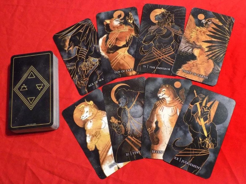 Puede incluir: Una baraja de cartas de tarot con dise&ntilde;os en negro y dorado. Las cartas presentan ilustraciones de animales y criaturas m&iacute;ticas. Las cartas est&aacute;n dispuestas sobre una superficie roja. Las cartas incluyen el As de la Guerra, el Diez de la Tierra, la Fuerza XI, el Emperador IV, el Tres de la Tierra, el Siete y el Juicio XX.
