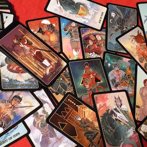 May include: A spread of tarot cards with black borders and gold accents. The cards feature colorful illustrations of people, animals, and symbols. The cards are laid out on a red surface.