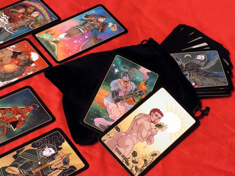 May include: A set of tarot cards with colorful illustrations and gold accents. The cards are spread out on a red surface with a black velvet bag and a stack of cards in the background.