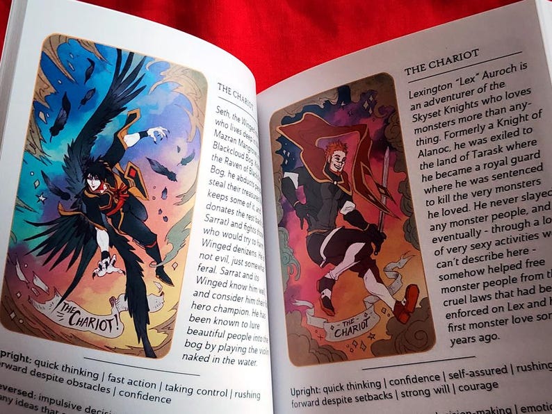 Pu&ograve; includere: Libro aperto con due illustrazioni di un mazzo di tarocchi fantasy. Uno mostra una figura alata in nero e arancione, etichettata "Il Carro". L'altro raffigura una figura dai capelli rossi con una spada, anch'essa "Il Carro".