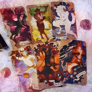 Pu&ograve; includere: Un set di carte dei tarocchi con illustrazioni fantasy. Le carte raffigurano creature mitiche, tra cui un demone alato, un satiro e un lupo mannaro. Ogni carta ha un design unico con titoli come "Giudizio" e "Nove di Spade."