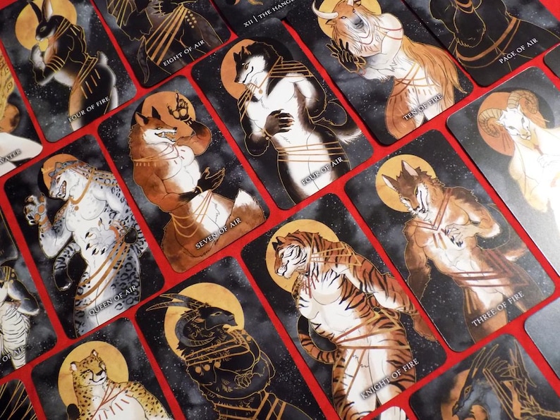 Puede incluir: Un juego de cartas de tarot con ilustraciones de animales antropomorfos en varias poses. Las cartas est&aacute;n decoradas con detalles dorados y tienen un fondo negro con un patr&oacute;n estrellado. Las cartas incluyen los siguientes t&iacute;tulos: "Four of Fire", "Eight of Air", "XII The Hang", "Queen of Air", "Seven of Air", "Page of Air", "Knight of Fire" y "Three of Fire".