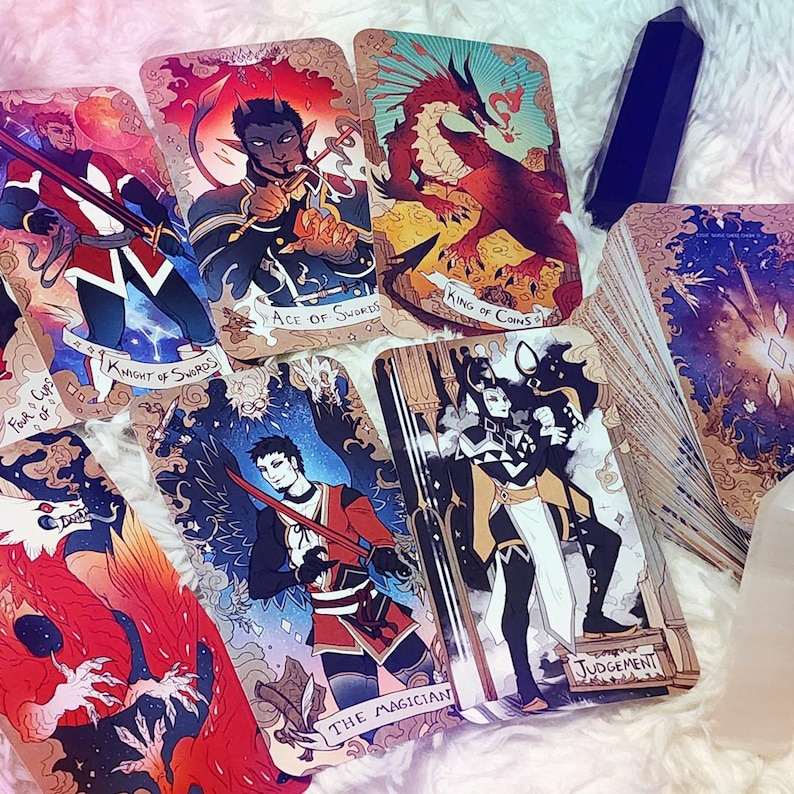 Pu&ograve; includere: Una collezione di carte dei tarocchi con illustrazioni fantasy, tra cui il Cavaliere di Spade, l'Asso di Spade, il Re di Denari, Il Mago e il Giudizio. Le carte presentano opere d'arte dettagliate con colori vivaci, disposte su una superficie bianca e morbida.