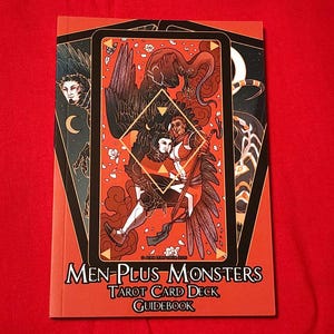 May include: A red guidebook with the title "Men-Plus Monsters Tarot Card Deck Guidebook" and an illustration of two figures with wings on the cover.