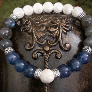 May include: A bracelet made with white, grey, and blue beads. The bracelet has silver accents and is made with natural stones.