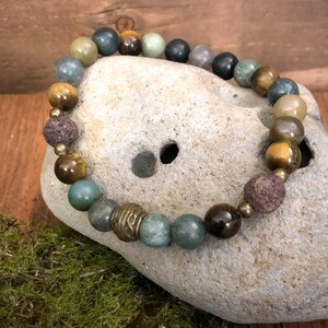 May include: A beaded bracelet with green, brown, and black beads. The bracelet is made with natural stones and lava beads.