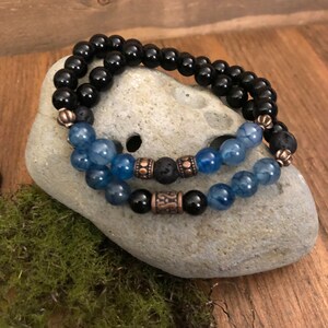 Puede incluir: Dos pulseras con cuentas negras y azules. La pulsera superior está hecha de cuentas negras y la pulsera inferior está hecha de cuentas azules y negras con detalles en cobre.