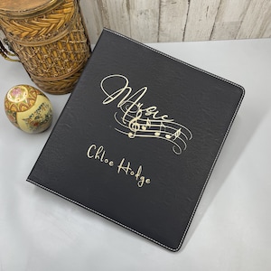 May include: Black leather binder with gold musical notes and the text "Music" and "Chloe Hodge".