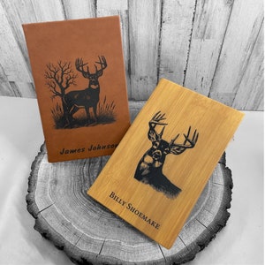 May include: Two personalized leather journals with a deer silhouette design. The brown journal has the name "James Johnson" engraved on it. The beige journal has the name "Billy Shoemaker" engraved on it.