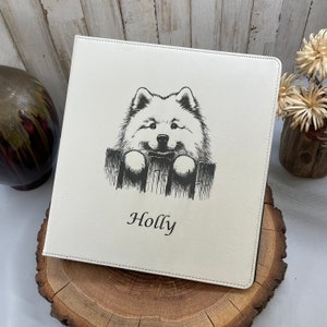 May include: White leather photo album with a black and white illustration of a dog peeking over a fence. The album is personalized with the name "Holly".