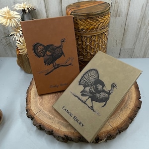 May include: Two brown leather journals with a turkey design and the names "Stanley Hester" and "Lance Riley" printed on the front.