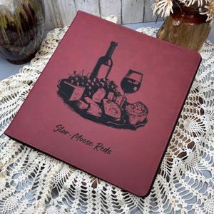 May include: A red leather-bound journal with a black and white illustration of a wine bottle, grapes, cheese, and a glass of wine. The text "Star-Moose Reds" is printed on the cover.