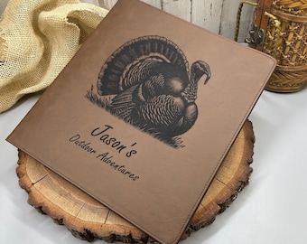 May include: A brown leatherette binder featuring a black laser-engraved image of a turkey. The text "Jason's Outdoor Adventures" is engraved in black below the turkey. The binder has stitched edges and a smooth, textured surface.