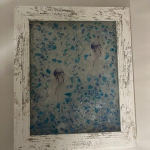 May include: A white framed picture with a blue and green background of small glass pieces. Two purple jellyfish are depicted in the picture.