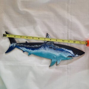 May include: A blue and white shark wall art sculpture with a black outline. The shark is approximately 13 inches long.