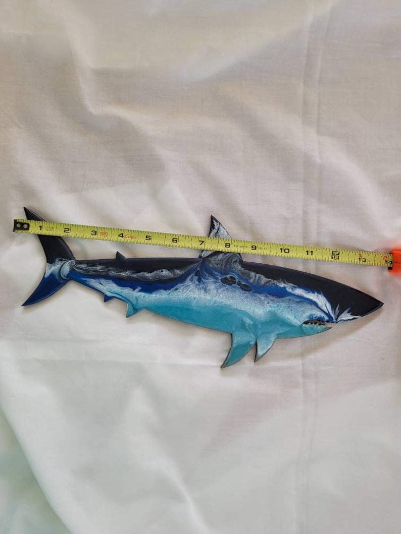 May include: A blue and white shark wall art sculpture with a black outline. The shark is approximately 13 inches long.