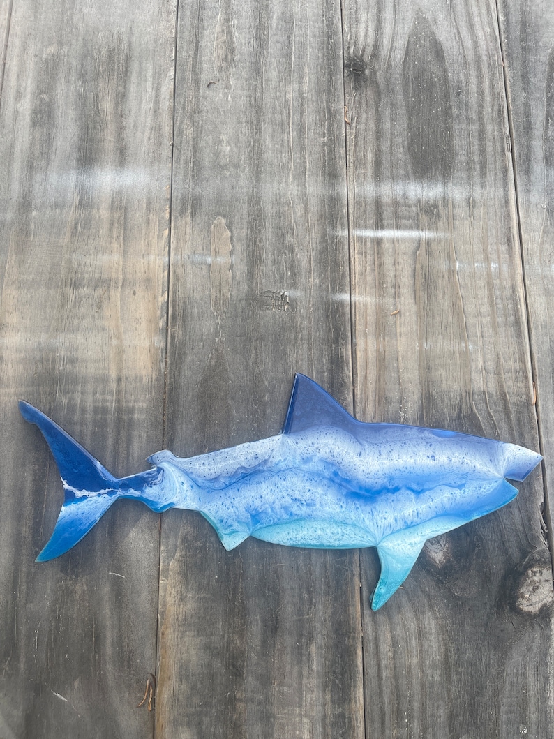 May include: A blue and white resin shark wall decor. The shark is in a side profile with its mouth open. The shark is painted with a blue and white marbled effect.