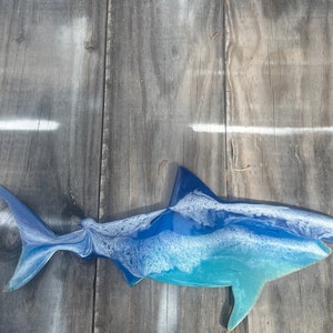 May include: A blue and white resin shark sculpture with a white background. The shark is facing left and has a detailed, textured surface.