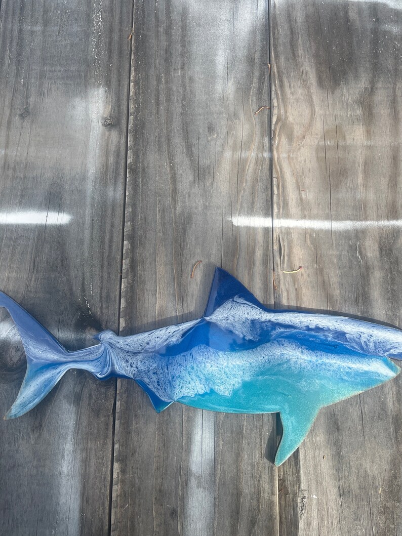 May include: A blue and white resin shark sculpture with a white background. The shark is facing left and has a detailed, textured surface.