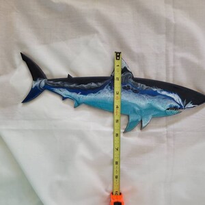 May include: A blue, white, and black painted wooden shark wall decor measuring approximately 10 inches in length.