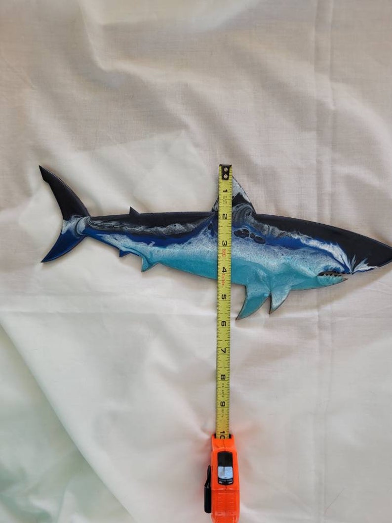 May include: A blue, white, and black painted wooden shark wall decor measuring approximately 10 inches in length.