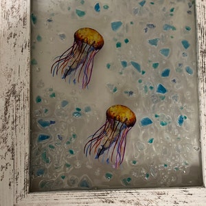 May include: A framed artwork featuring two yellow jellyfish with purple tentacles against a white background with blue and green glass pieces.