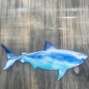 May include: A blue and white resin shark wall sculpture. The shark is in a side profile with its mouth closed. The sculpture is mounted on a wooden background.