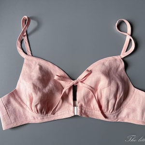 Peut inclure: Une bralette rose clair dotée d'une fermeture à l'avant, de fines bretelles réglables et d'un petit nœud décoratif au centre de l'encolure. Le vêtement présente une finition en tissu texturé et inclut le texte The little Heidi.