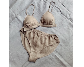 Op de afbeelding: Een tweedelige set bestaande uit een beige driehoekige bralette met dunne verstelbare schouderbandjes en een bijpassende high-waisted slip met een elastische tailleband, gemaakt van een textuurrijke stof met een zichtbaar weefpatroon.
