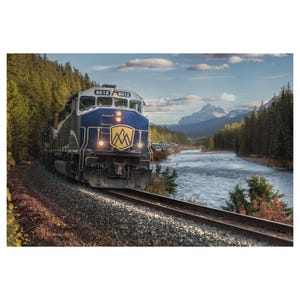 May include: A blue and gold train engine with the number 8012 on the side, traveling through a mountain valley with a river running through it.