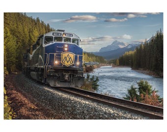 May include: A blue and gold train engine with the number 8012 on the side, traveling through a mountain valley with a river running through it.
