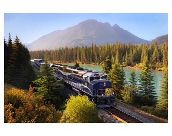 May include: A scenic photograph of a blue and gold train, labeled "Rocky Mountaineer," traveling along a track beside a turquoise lake. The train is surrounded by lush green trees and a mountain range under a clear blue sky.