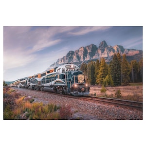 May include: A green and gold train engine with the words "Rocky Mountaineer" on the side, traveling through a mountain range with a forest in the foreground.