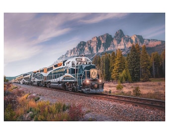 May include: A green and gold train engine with the words "Rocky Mountaineer" on the side, traveling through a mountain range with a forest in the foreground.