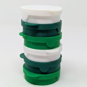 May include: A stack of six round containers with white lids and green bases. The containers are stacked in alternating colors, with the white lids on top.