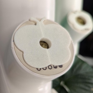 May include: White plastic butterfly-shaped bottle stopper with a hole in the center. The stopper has a textured surface and is designed to fit on a bottle.