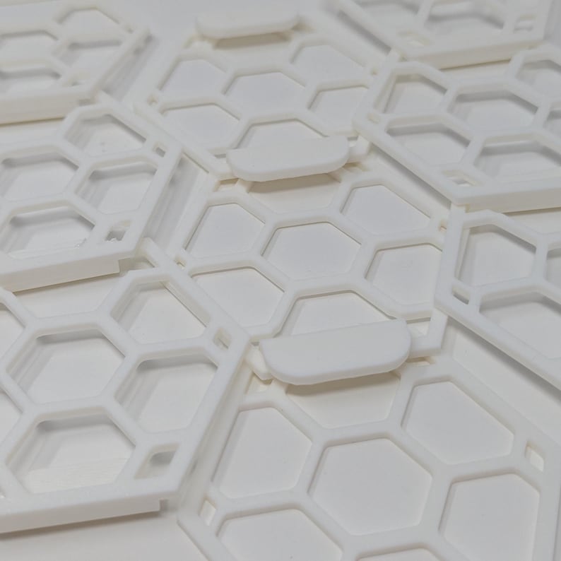 May include: A close-up of white plastic honeycomb-shaped tiles stacked on top of each other. The tiles have a raised edge around the perimeter.