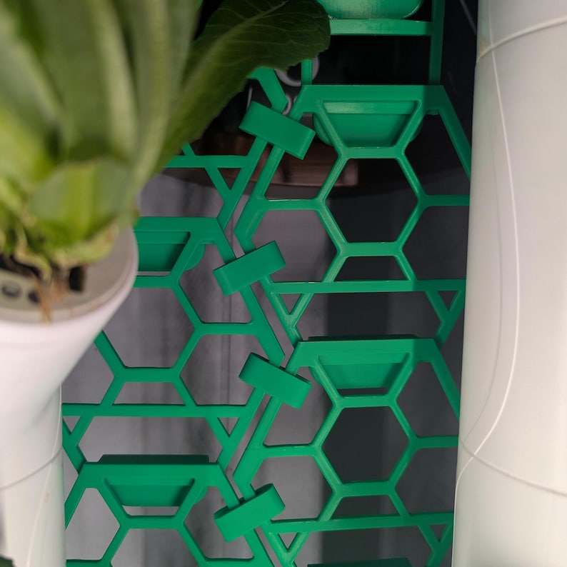 May include: Green plastic honeycomb-shaped panel with a series of small, rectangular tabs. The panel is attached to a white surface.