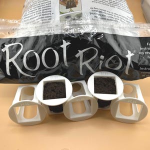May include: A package of Root Riot plant starter cubes with a bag of rooting material. The white cubes are arranged in a row, each holding a square of dark brown growing medium. The bag has the words "Root Riot" in large white letters.