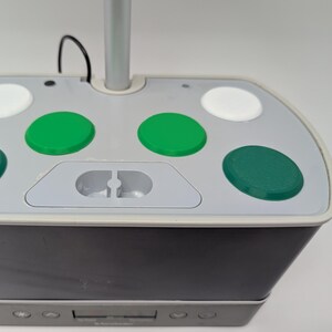 May include: Close-up of a gray and black indoor garden system. The top has several green and white circular buttons. A silver pole extends upwards from the center. The base has a dark gray exterior with a control panel.