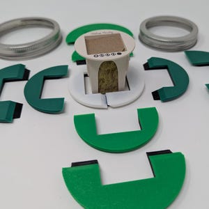 May include: A white coffee filter with a brown paper insert and the text "Drink Happy" on the front. The filter is surrounded by eight green plastic pieces that form a circle.