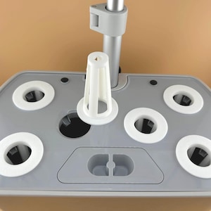 May include: A close-up of a gray hydroponic system base with white circular inserts and a white plastic cone-shaped plant holder. A silver pole is attached to the base. The system is designed for indoor gardening.