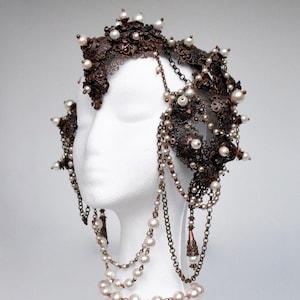 Può includere: Un copricapo delicato realizzato in metallo e perle. Il copricapo è adornato con dettagli intricati e presenta un design a corona. Il copricapo è indossato su un manichino bianco.