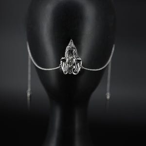 May include: A silver nose chain with a decorative, ornate pendant. The chain is attached to two dangling pieces that hang down from the nose.