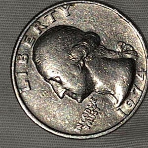 May include: A silver US quarter dollar coin with the year 1975 and the words "Liberty" and "In God We Trust" inscribed on it.