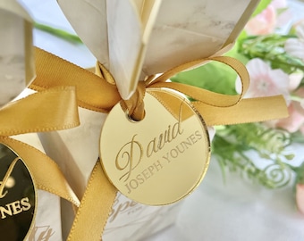 May include: A gold favor box with a gold ribbon and a round gold mirror tag with the name "David Joseph Younes" engraved on it.