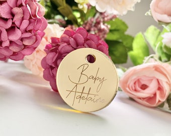 May include: Gold round tag with the text "Baby Adelaide" written in cursive.
