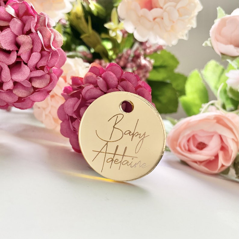 May include: Gold round tag with the text "Baby Adelaide" written in cursive.
